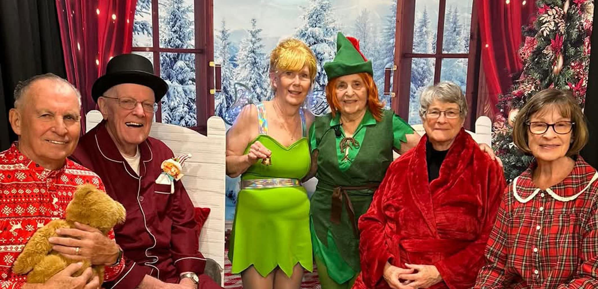 Residents at The Villas at Stoney Point dressed in festive costumes for their "Peter Pan" performance, posing together in front of a winter-themed backdrop with joyful expressions.