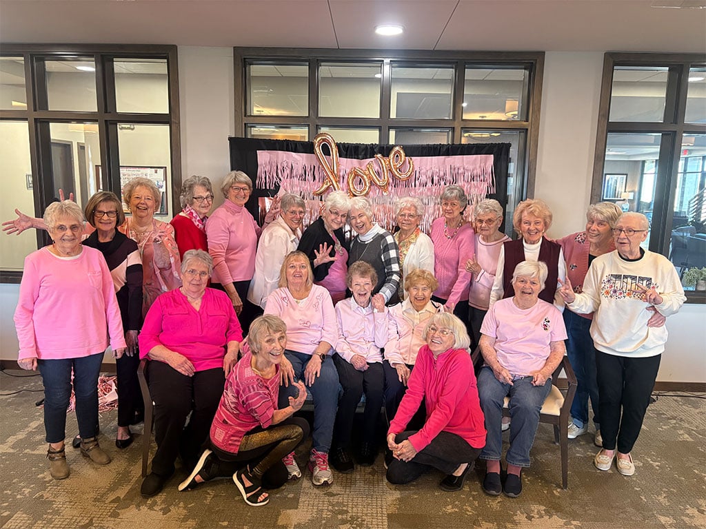 Large group of residents celebrating Galentine’s Day at Villas at Stoney Point, wearing pink and posing in front of a festive “Love” backdrop.
