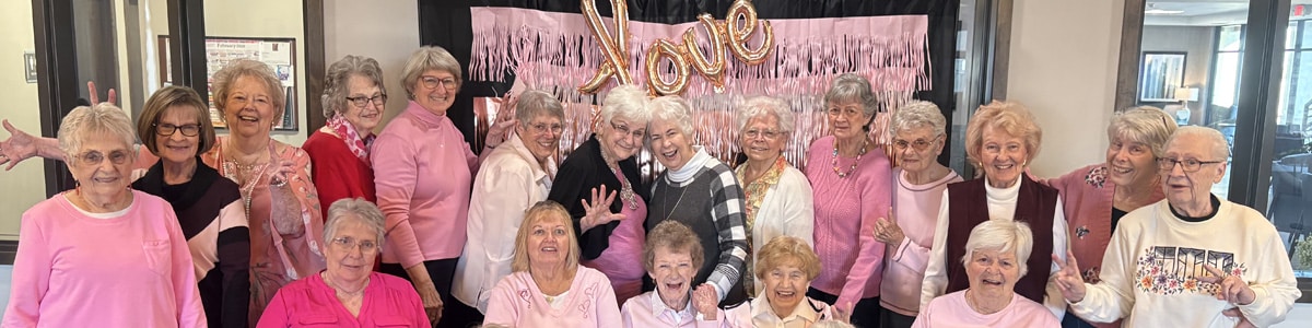 Group of women at Villas at Stoney Point wearing pink and gathered in front of a “Love” backdrop during a Galentine’s Day celebration.