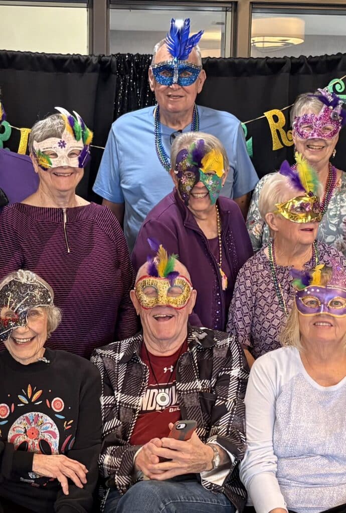 Residents at Villas at Stoney Point wearing Mardi Gras beads and feathered accessories during the community’s annual Fat Tuesday celebration.