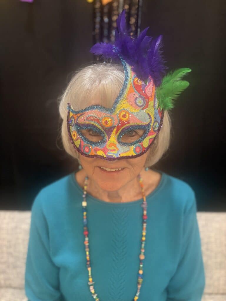Resident at Villas at Stoney Point wearing a colorful feathered Mardi Gras mask and beads during the Fat Tuesday festivities.