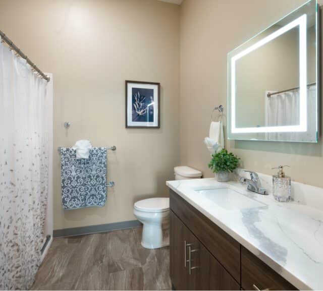 Apartment bathroom with vanity sink, illuminated mirror, toilet, and tub shower combination at Villas at Stoney Point
