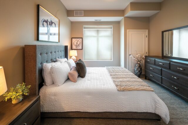 Apartment bedroom with bed, dresser, nightstands, artwork, and window at Villas at Stoney Point
