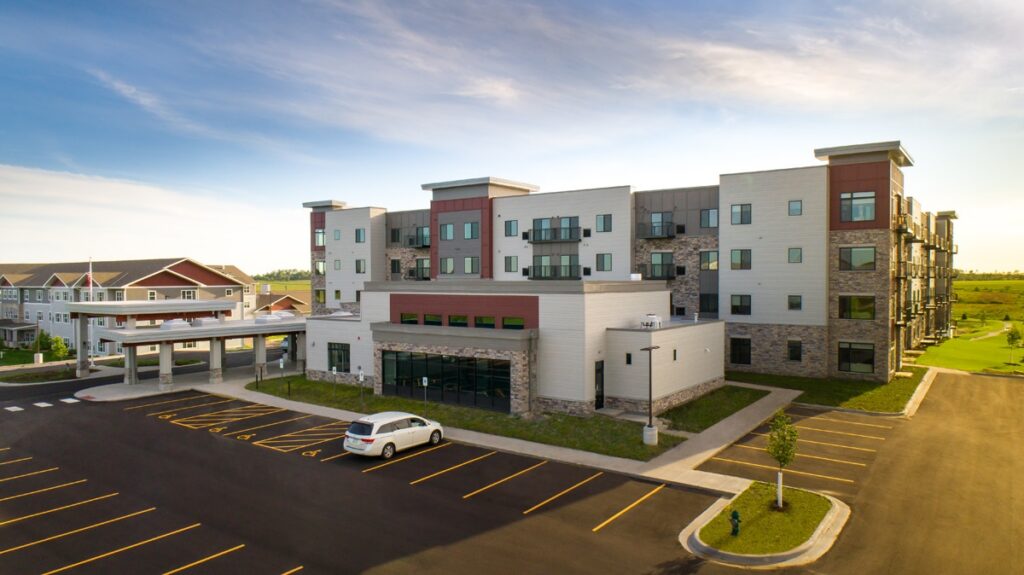 Aerial view of Villas at Stoney Point showing the main building entrance, covered drop-off area, parking lot, and surrounding landscape