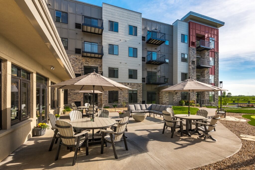 Outdoor courtyard patio with tables, chairs, umbrellas, and seating area beside the apartment building at Villas at Stoney Point