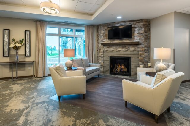 Comfortable lounge seating area with armchairs, sofa, stone fireplace, wall-mounted television, and large window at Villas at Stoney Point