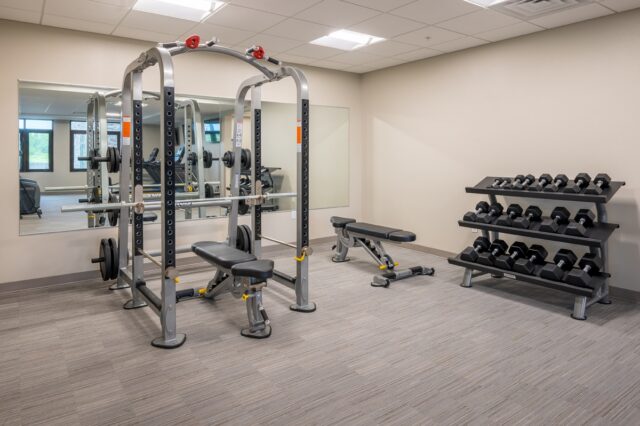 Fitness center with weight training equipment, adjustable bench, dumbbell rack, and wall mirrors at Villas at Stoney Point