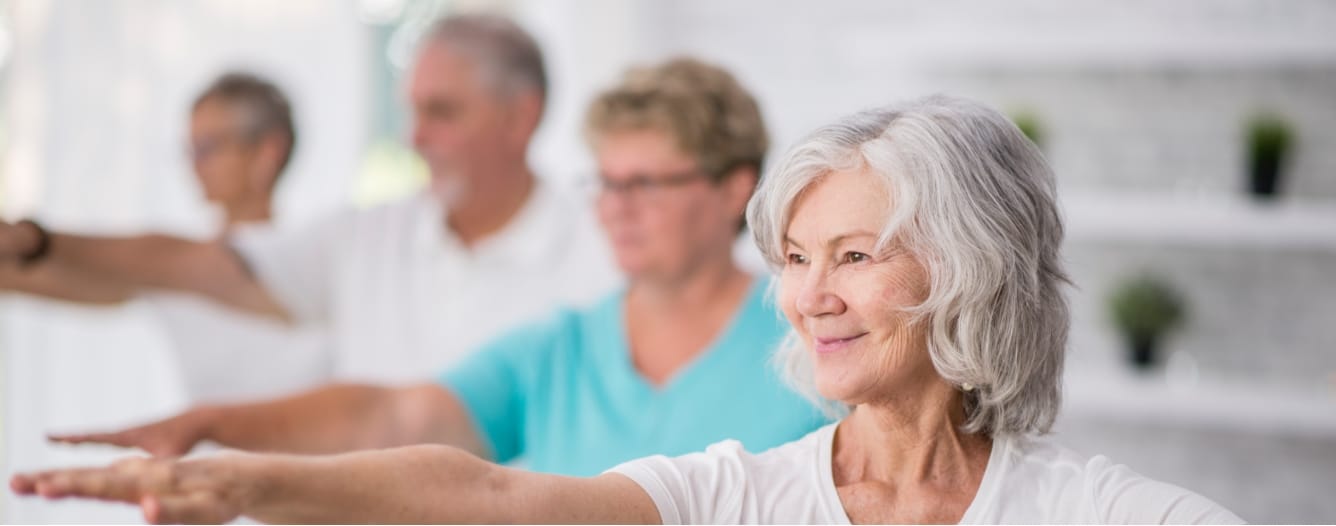 Group of older adults participating in a light exercise class with arms extended, representing wellness and fitness activities like Villas at Stoney Point