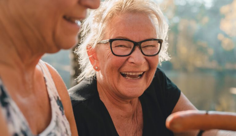 Adult smiling outdoors while seated near water with another person nearby, representing an active and social lifestyle like Villas at Stoney Point