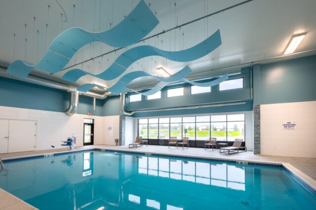 Indoor swimming pool with lounge chairs, large windows, and high ceilings with decorative panels at Villas at Stoney Point