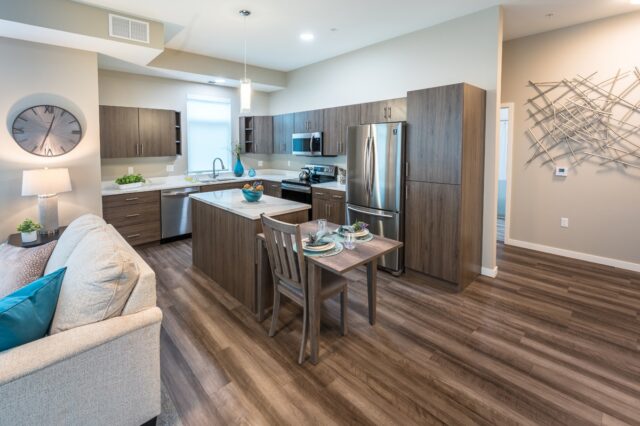 Apartment kitchen with island, dining table for two, stainless steel appliances, and wood cabinetry in an open layout at Villas at Stoney Point