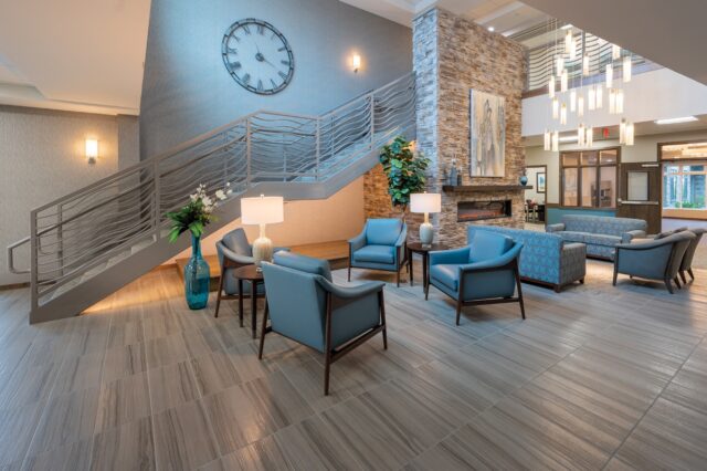 Lobby seating area with armchairs, side tables, staircase, large wall clock, fireplace, and decorative lighting at Villas at Stoney Point