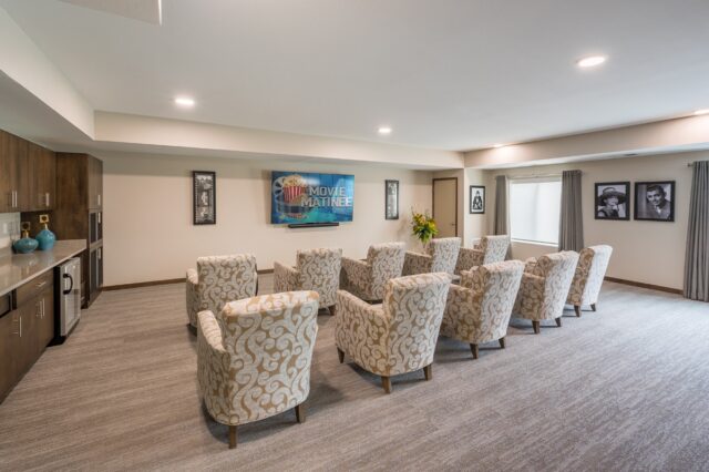 Movie viewing room with multiple upholstered chairs arranged facing a television, along with a kitchenette area at Villas at Stoney Point