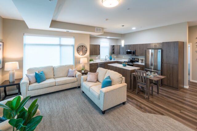 Open-concept apartment with living room seating, kitchen with island, dining table, and modern appliances at Villas at Stoney Point