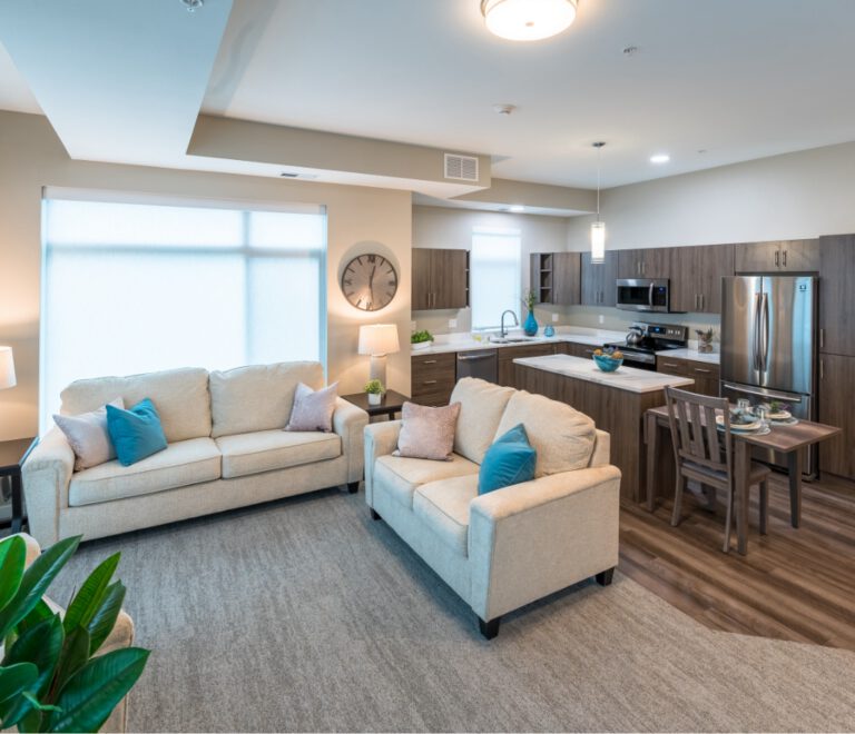 Open-concept apartment with living room seating, kitchen with island, dining table, and large window for natural light at Villas at Stoney Point