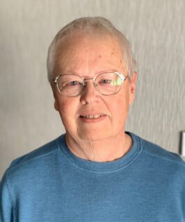 Close-up portrait of an adult in an indoor setting with neutral background, representing a welcoming senior living lifestyle like Villas at Stoney Point