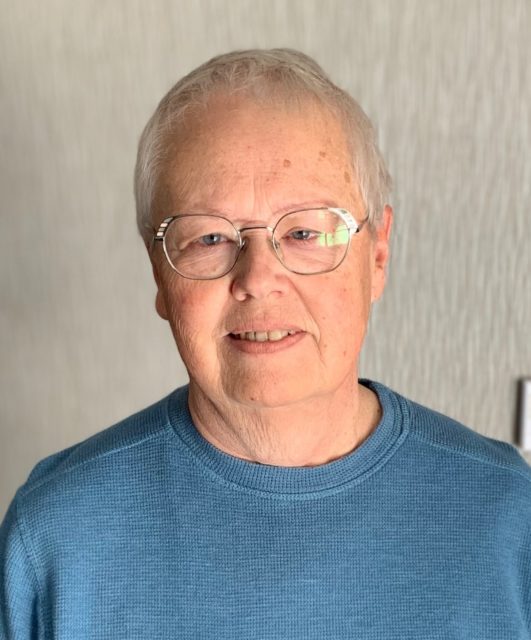 Close-up portrait of an adult in an indoor setting with neutral background, representing a welcoming senior living lifestyle like Villas at Stoney Point