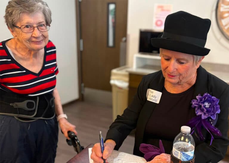 Resident in period costume signs a document during the America 250 celebration at Villas at Stoney Point, as another resident looks on.