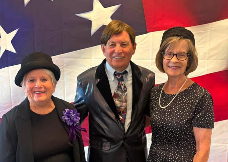 Three residents in vintage-inspired attire pose in front of an American flag backdrop during the America 250 celebration at Villas at Stoney Point.