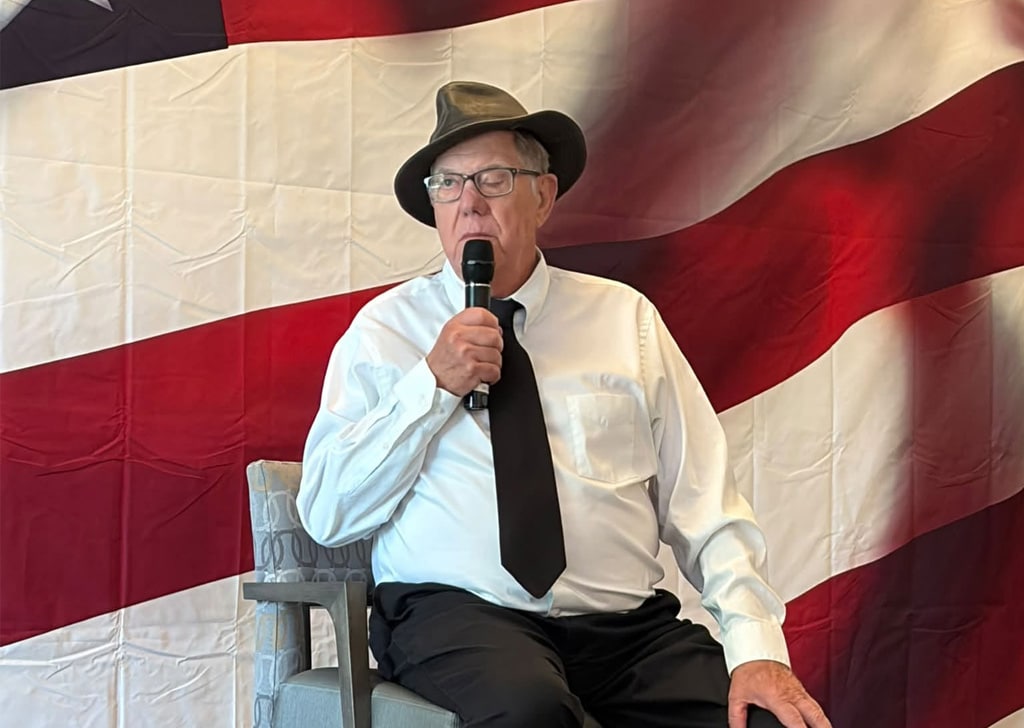 Resident in costume speaks into a microphone in front of an American flag backdrop during the America 250 celebration at Villas at Stoney Point.