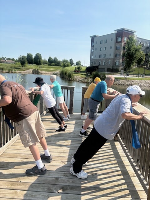 Group of residents doing resistance band exercises on a boardwalk overlooking a pond.