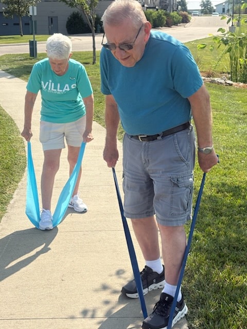 Two residents using resistance bands while exercising on a sidewalk outdoors.