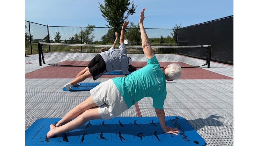 Residents doing side plank exercises on mats during an outdoor fitness class.